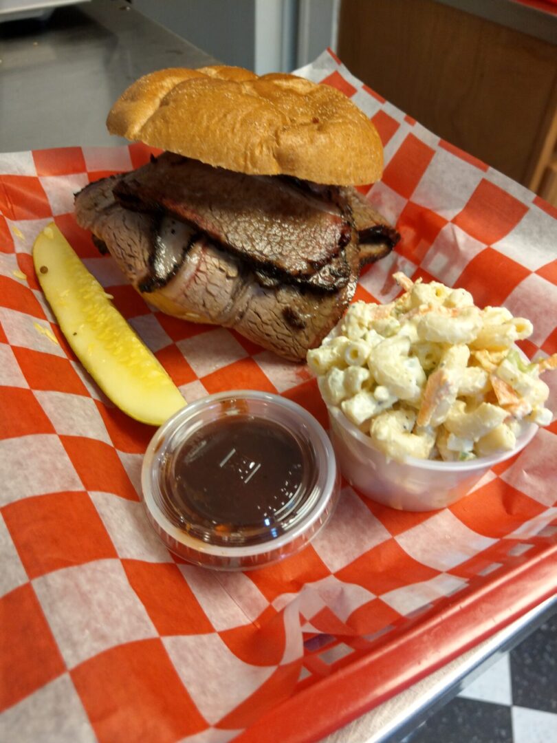 A sandwich, pickle and macaroni salad on a red checkered tray.