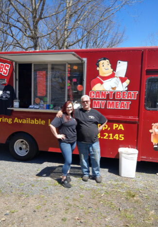 A couple standing in front of a food truck.