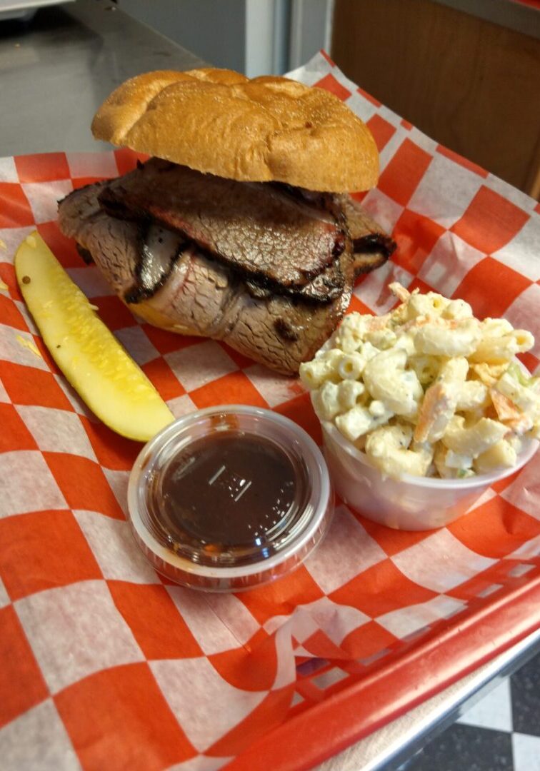 A sandwich, pickle and macaroni salad on a red checkered tray.